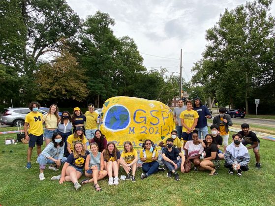 20+ GSP students stand by their newly painted UofM rock, a yearly tradition. The rock reads “GSP 2021-2022” and depicts a globe.
