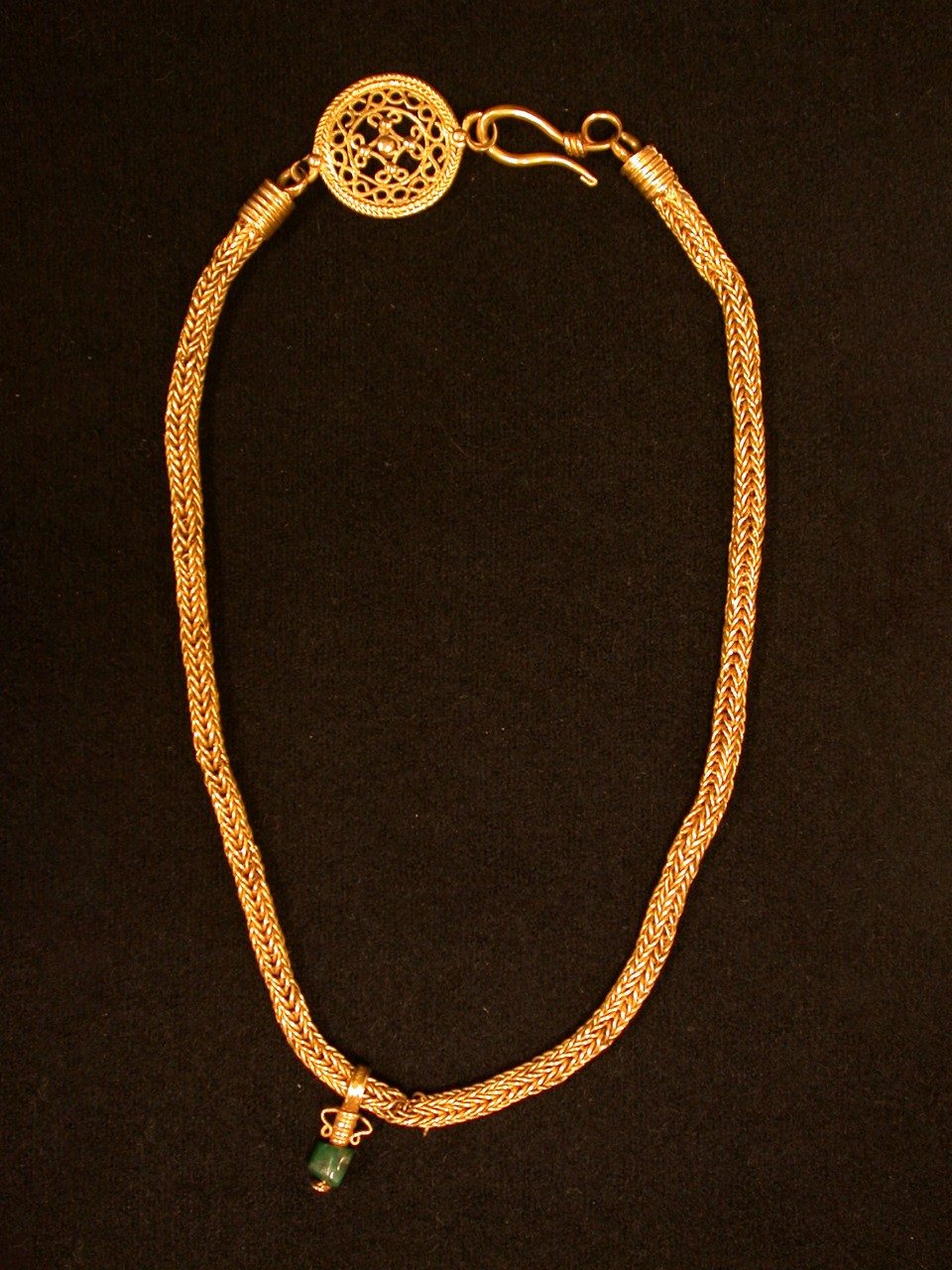 A thick-chained gold necklace with a dangling emerald pendant and ornamental clasp.
