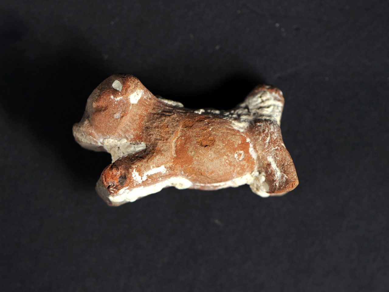 Small, red clay dog figurine with its legs stretched as though running.