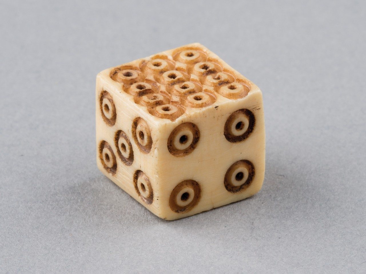 Six-sided bone die showing the 4, 5, and 12 sides. The pips are carved concentric circles.