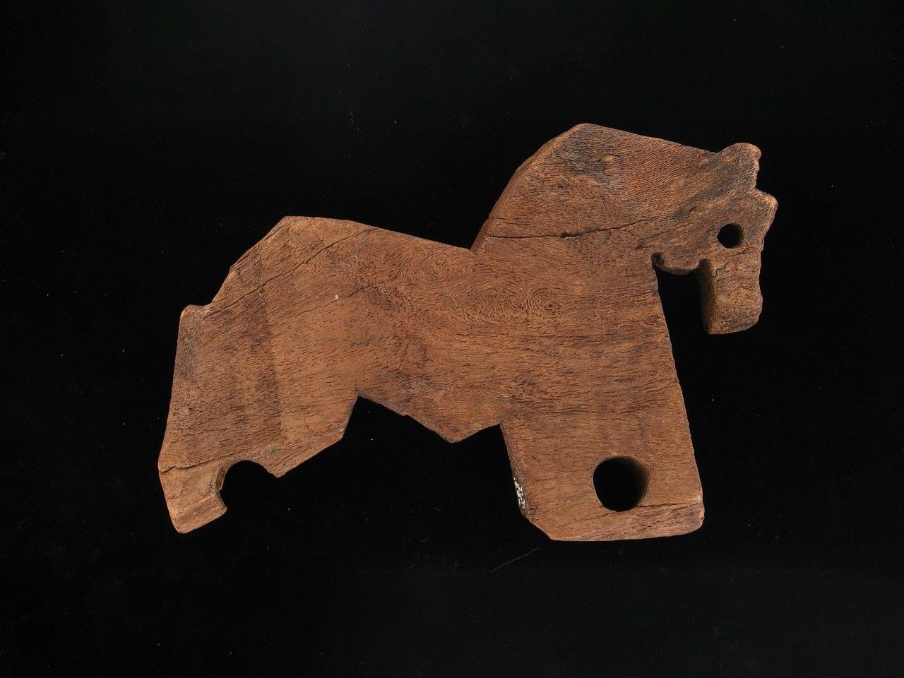 A 2-D horse shape carved from wood. There is a hole for the horse’s eye, as well as two large holes on its legs where wheels might have attached.