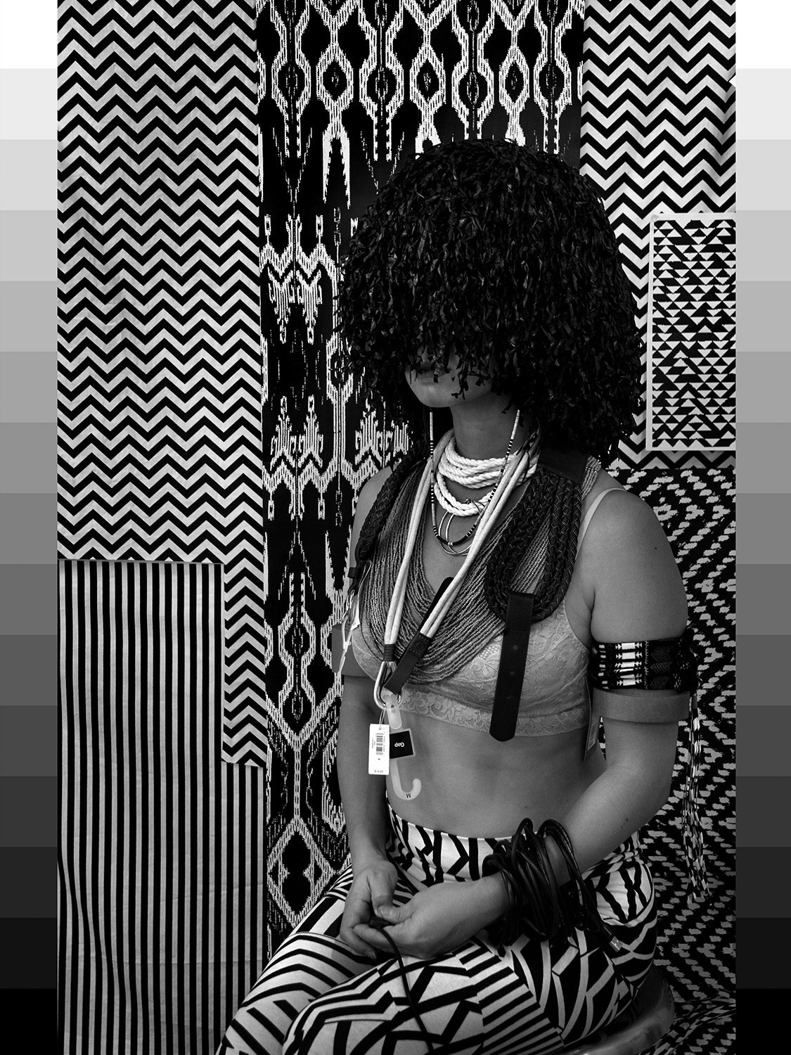 Woman in indigenous dress with something on her head covering her eyes, a hanger on her neck with a price tag in black and white