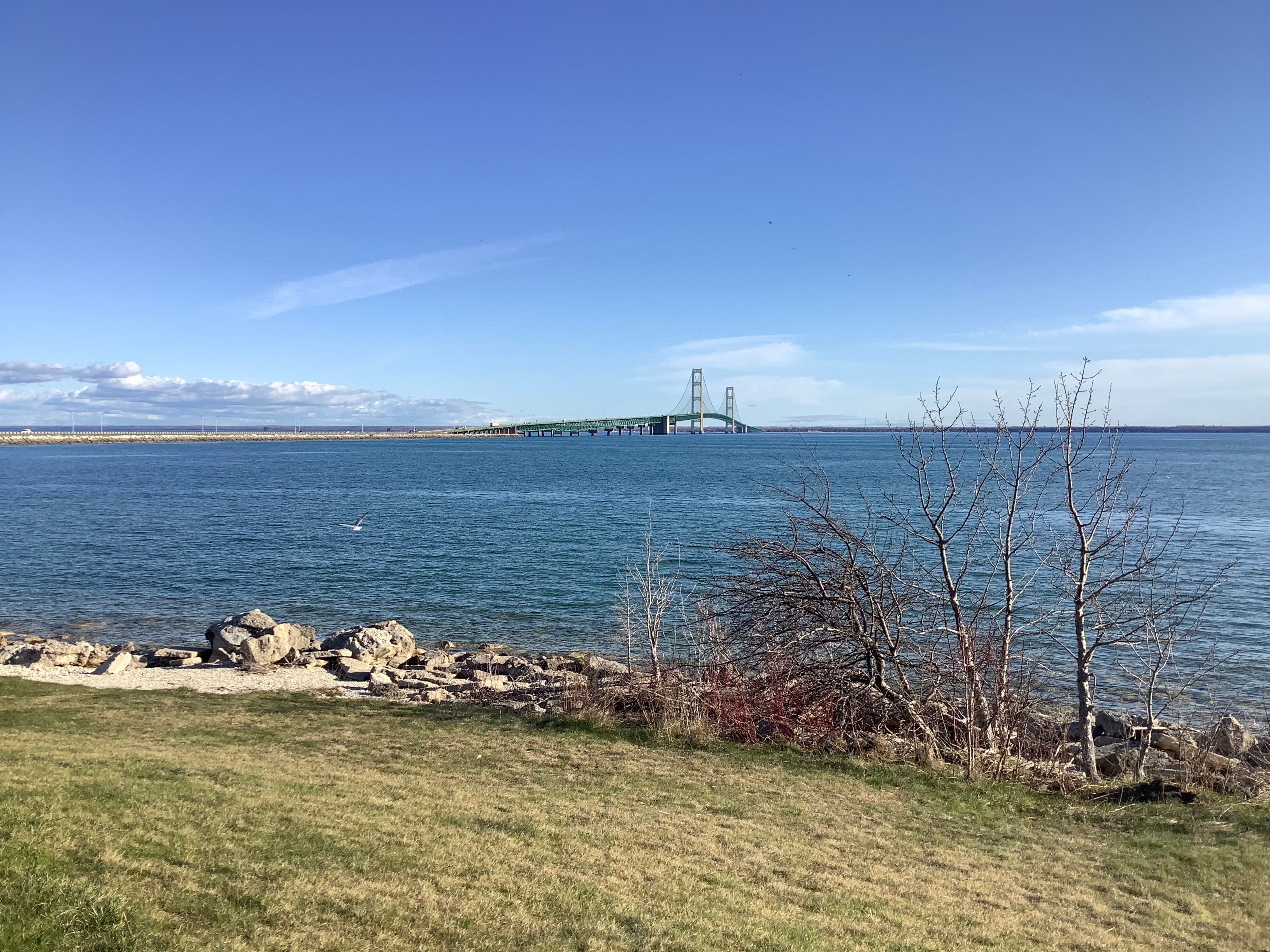 A view across the Straits of Mackinac, with the Mackinac Bridge far in the distance against a blue sky