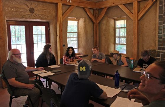 A professor and his students sit at tables in the straw bale building.