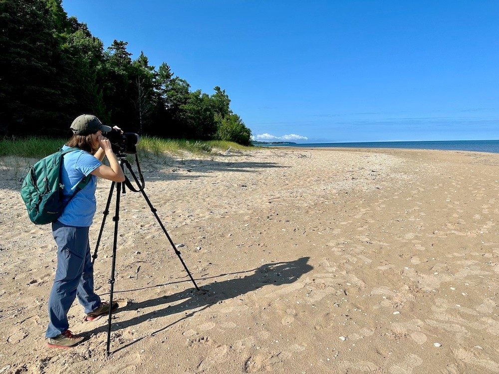 Woman looking through spotting scope on beach