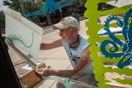 Cogswell affixing Unseen Worlds graphics on UMMNH windows