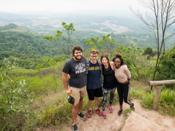 Photo of 4 young adults in Brazil posing for a photo with a lush green overlook behind them.