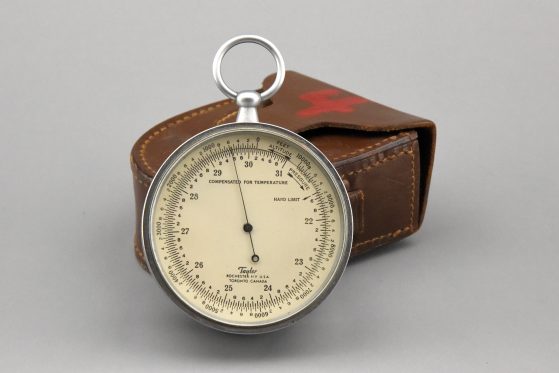 Photograph of round chrome and glass instrument with dial and hand leaned against leather carrying case, photo by Dale Austin