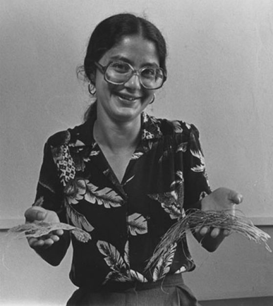 Deborah Goldberg circa 1980s, wearing large glasses, smiling, holding plants up in her hands.