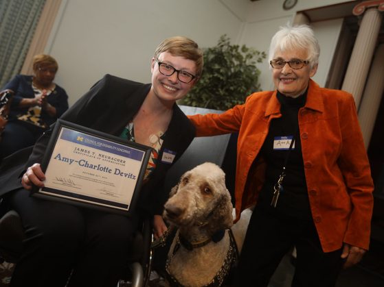 Amy-Charlotte Devitz (with her service dog, Fish) receives her award from Anna Schnitzer, chair, James T. Neubacher Awards Committee and informationist, Taubman Health Sciences Library. Image credit: Kyle Keener, Michigan Photography