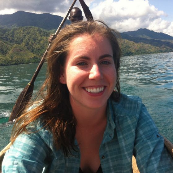 Joanna Larson on a boat with someone standing up rowing behind her, after snorkeling in Lake Malawi, Tanzania, to see cichlids. She was on a Fulbright (2012).