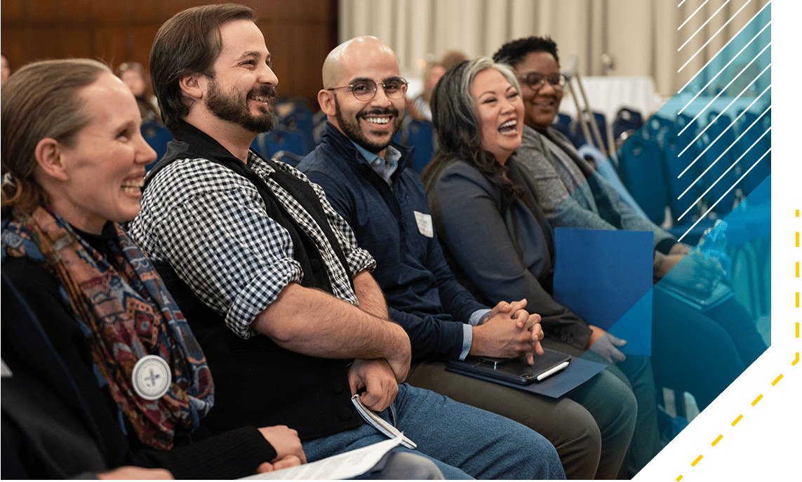 A photograph shows five people who spoke at a DEI event at the College of Literature, Science, and the Arts in 2023. They appear to be a diverse group of staff and faculty members. All are smiling broadly. The photo was taken inside a campus building in a ballroom. Four of the people look toward the stage, while one faces the camera.