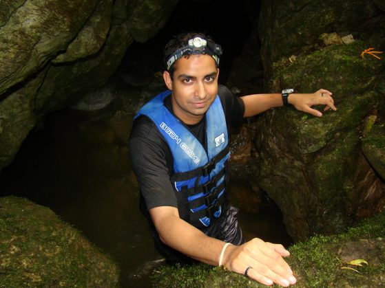 Prosanta Chakrabarty stands in a cave of moss-covered rocks. He wears a life vest and head lamp.