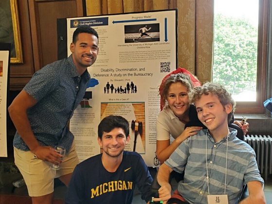 Vincent Pinti attends the Honors Summer Fellowship Presentation Seminar with three of his personal care assistants: Gianni Walker (B.S. ’21), James Kacsur (B.S. ’22), and U-M nursing student Caroline Dickerson. Pinti is in a wheelchair. Behind the group is a presentation board entitled “Disability, Discrimination, and Deference.”