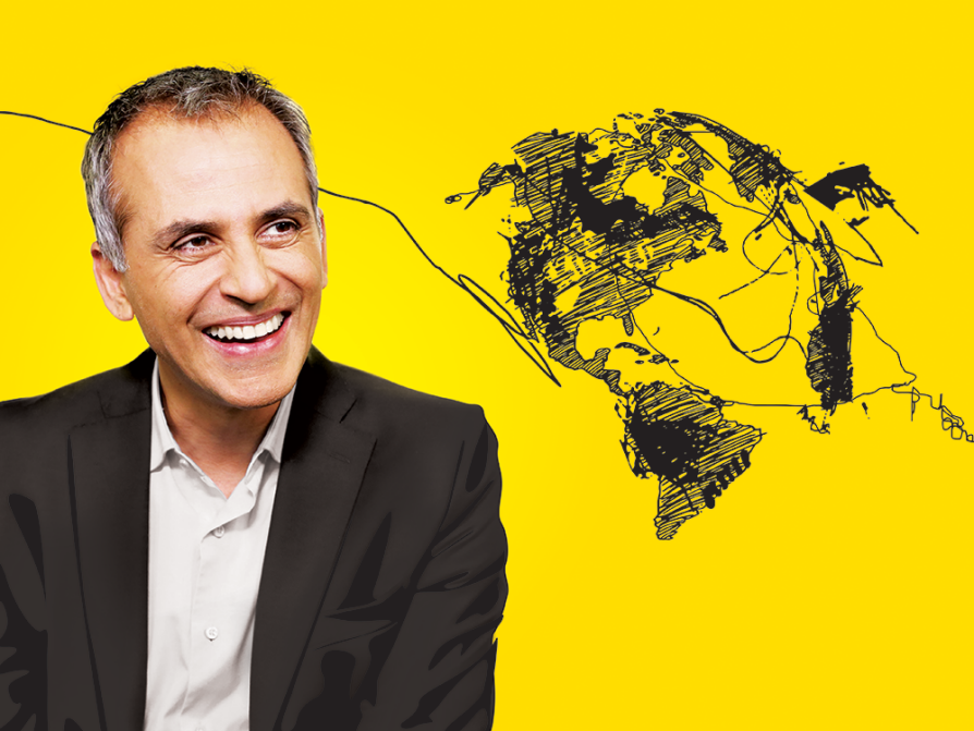 a photograph of Sanjay Varms wearing a dark coat and a light shirt looking to his left and laughing. The photo is against a yellow background, which has a rough drawing of the globe with disorganized squiggles and lines between the continents and going totally off the page in both directions.