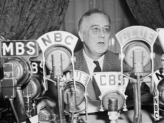 Black and white photograph of Franklin D Roosevelt speaking behind NBC, CBS and many other microphones.