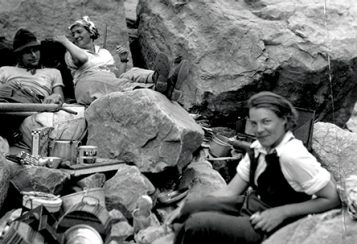 A depression-era photograph of two women, Elzada Clover and Lois Jotter, and two unidentified men sitting among big rocks with camping gear arrayed around them.
