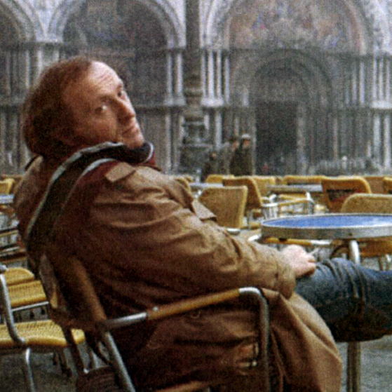 Joseph Brodsky sitting in an empty outdoor cafe looking back over his right shoulder.