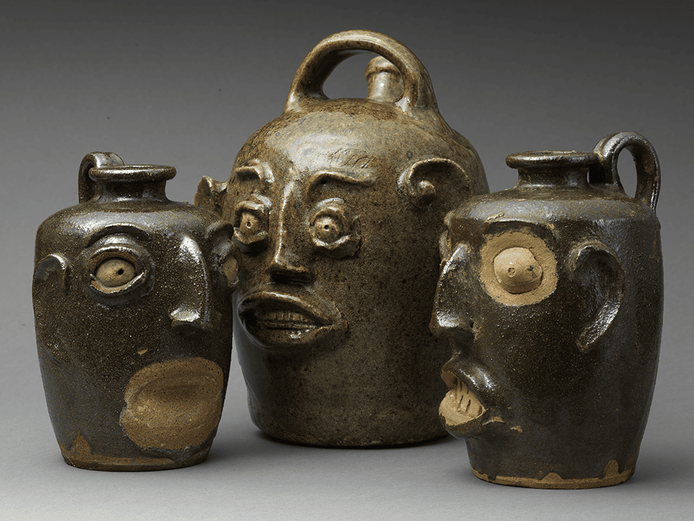 A photo of three ceramic face vessels facing toward a central point. Their eyes are at alternating levels and their mouths almost look ready to speak.