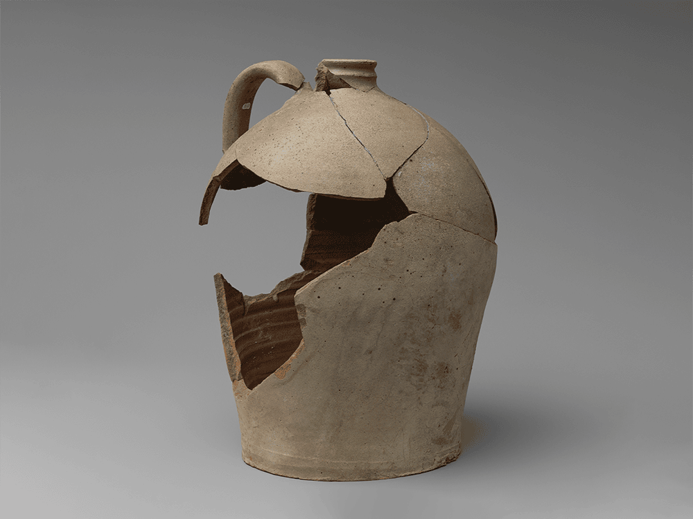 A beige broken jug is pieced back together in this photo. A large piece on it is still missing, leaving a hole and open space.