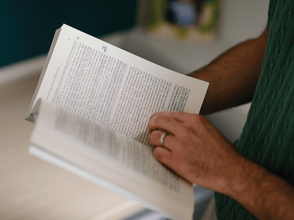In this photo, Professor Jeremy Levine’s hands hold a book open that has his notes throughout the pages in blue ink.