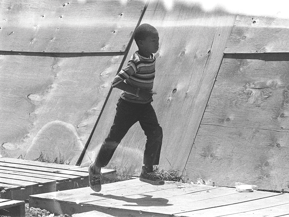 In this black-and-white photo, a young boy of color runs, both feet off the ground, outside in Washington, D.C.