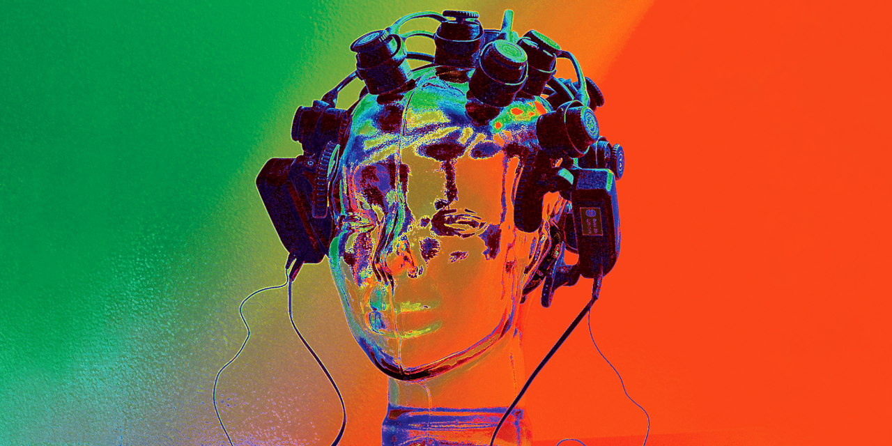 A mannequin head is placed on a table top with black head monitors all around it and black wires connecting them. The image is a vibrant dark green in the upper left corner, transitioning to a bright red and royal blue in the lower right corner. The image colors look similar to a thermal map.