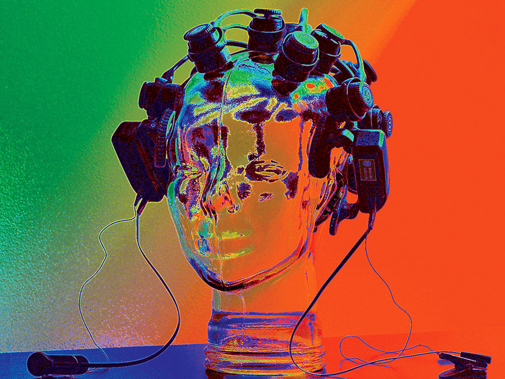 A mannequin head is placed on a table top with black head monitors all around it and black wires connecting them. The image is a vibrant dark green in the upper left corner, transitioning to a bright red and royal blue in the lower right corner. The image colors look similar to a thermal map.