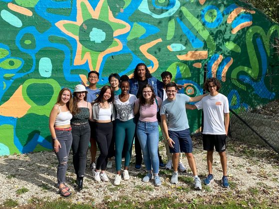 a group of 11 GSP students stand in front of a colorful wall mural on the Fall Colors Walk