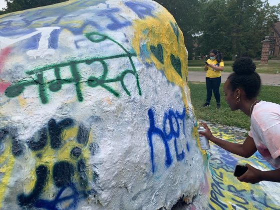 RA Sewit Yohannes paints on the UofM rock. In 2021, students chose to decorate and write greetings in multiple languages.