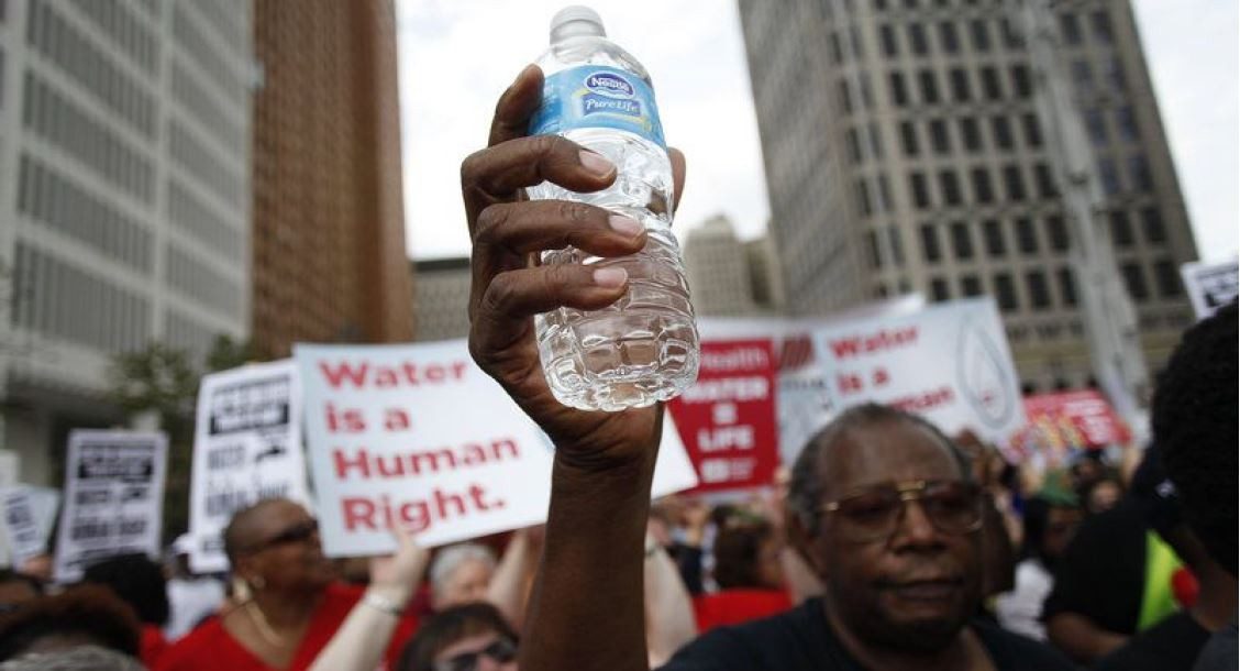 Man holding up a bottle of water in front of a crowd of protesters