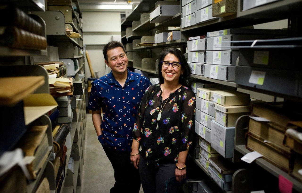 Professors Punzalan and de la Cruz stand in the middle of shelves containing archival materials at the Bentley Historical Library.