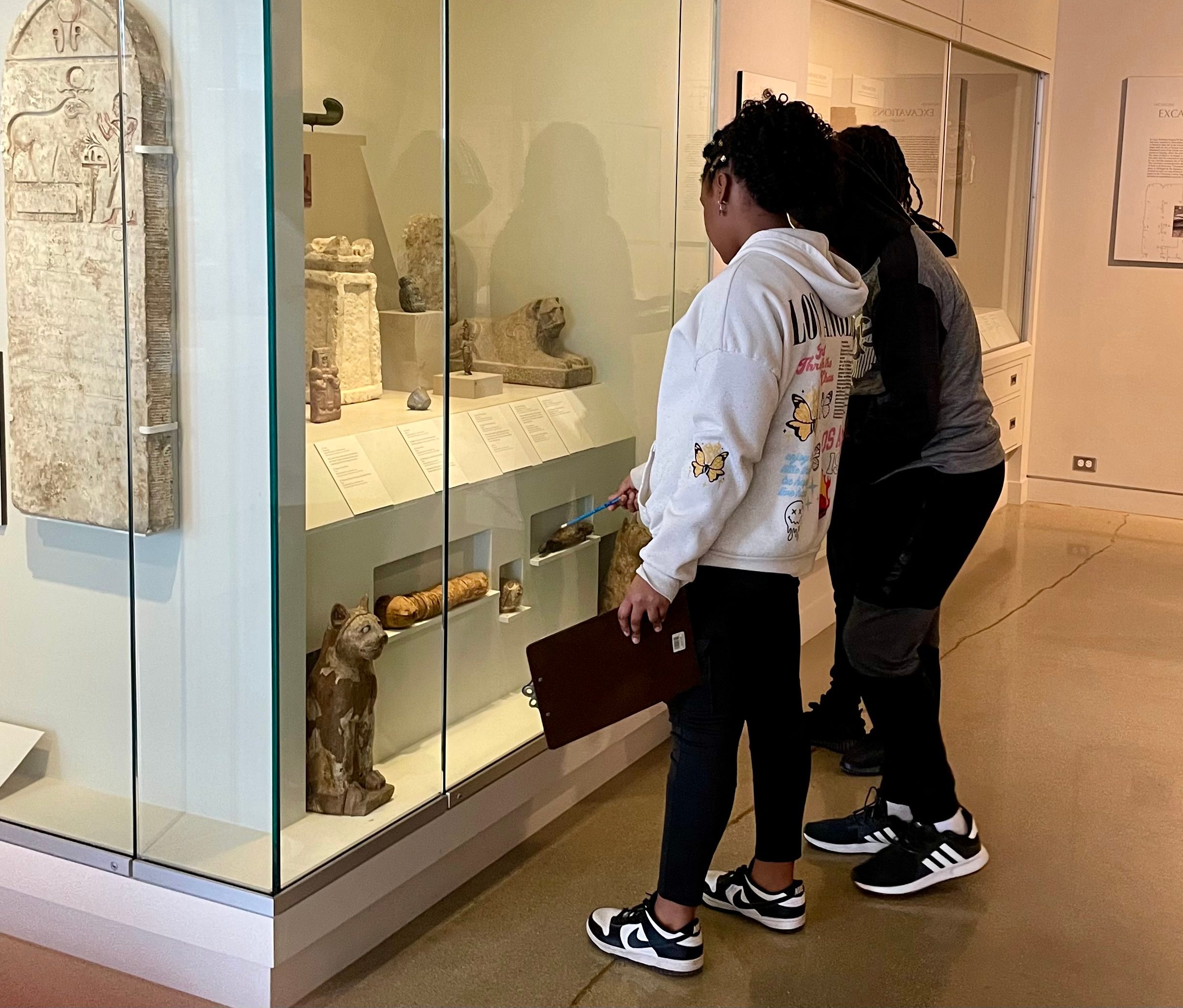 Middle school students look at artifacts in a Kelsey Museum vitrine.