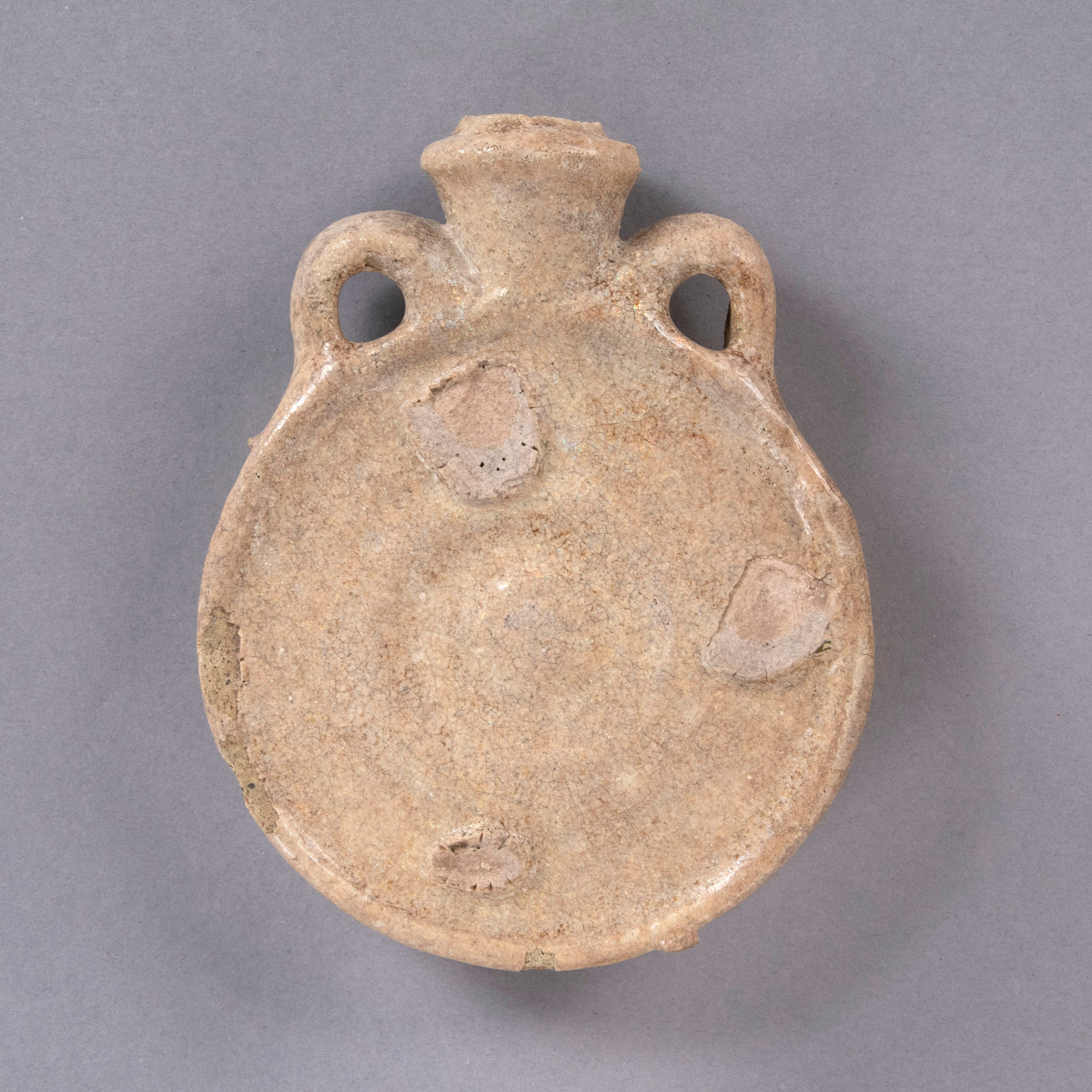 Tan, rounded pilgrim flask resembling a canteen. The object has two handles protruding near its spout.