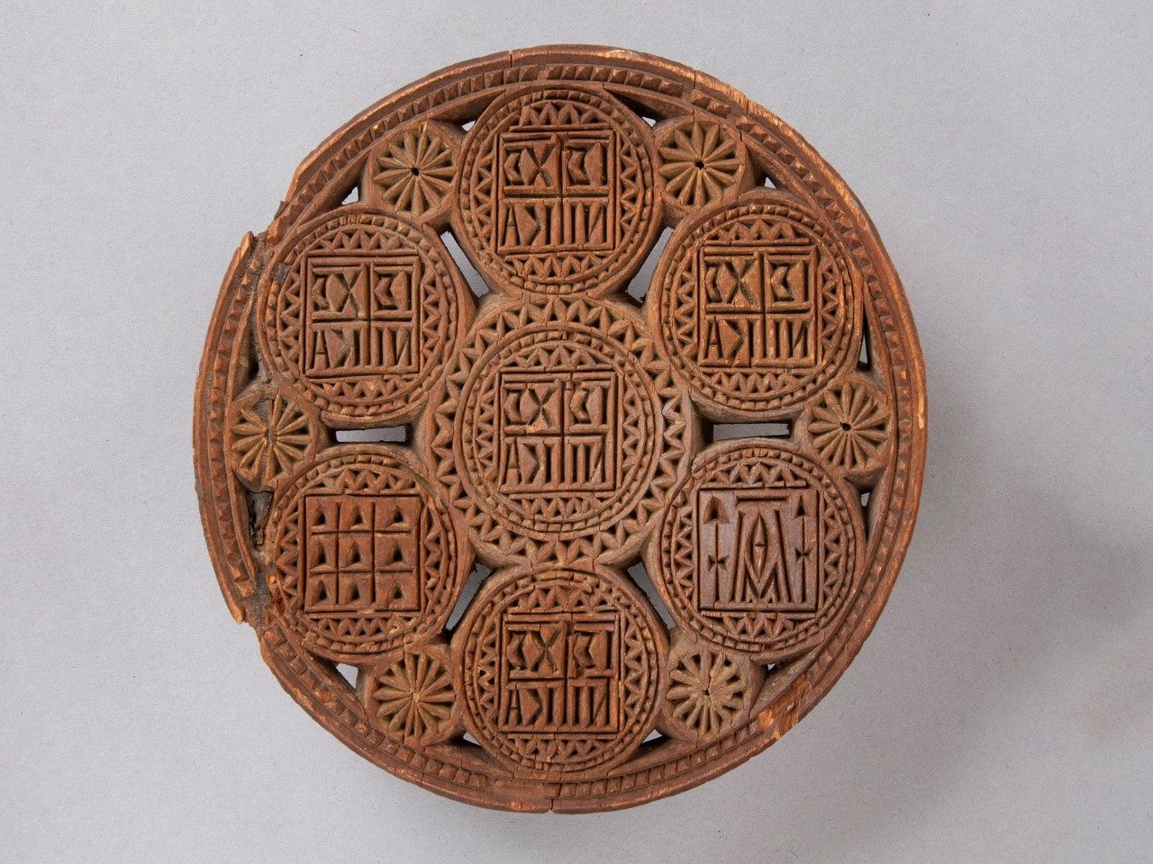 Intricately carved, round wooden seal consisting of several connected circles containing Christian symbols and motifs.