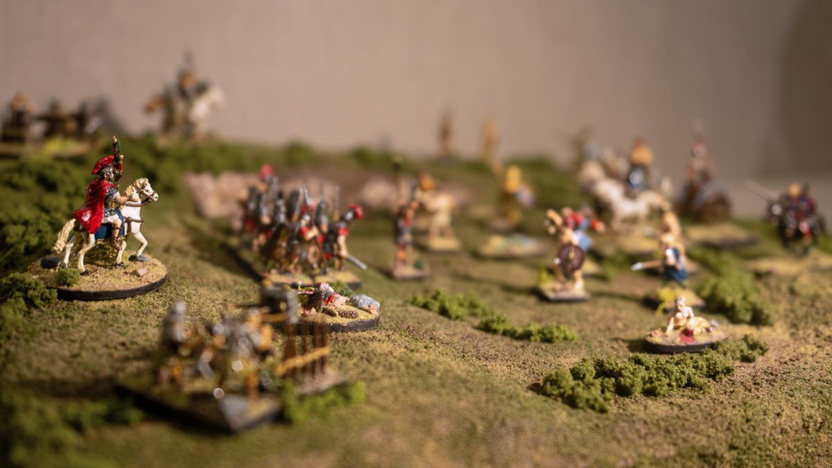 Diorama in a museum display showing a grassy battlefield with Roman soldiers, including horsemen and foot soldiers, on the left and Celts, with bow, arrow, and spears, on the right.