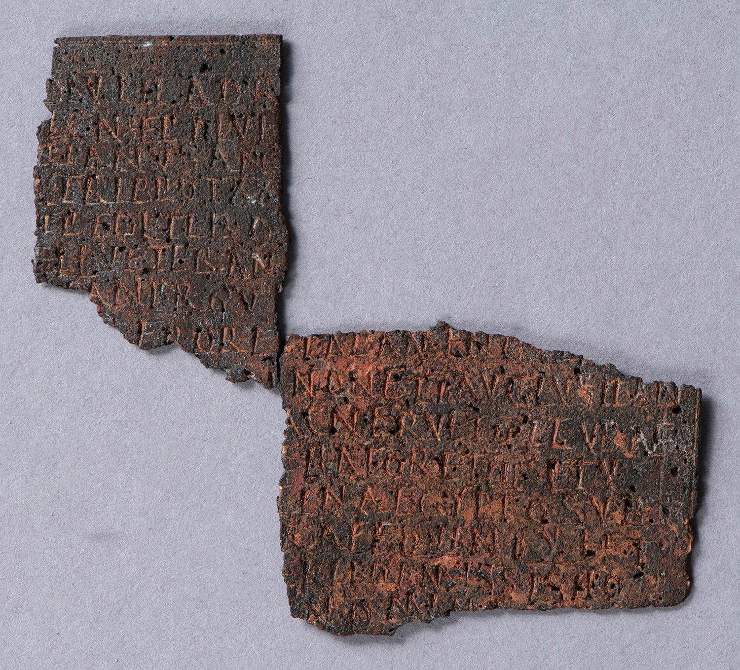 Two roughly rectangular pieces of rusted bronze with Latin inscriptions.