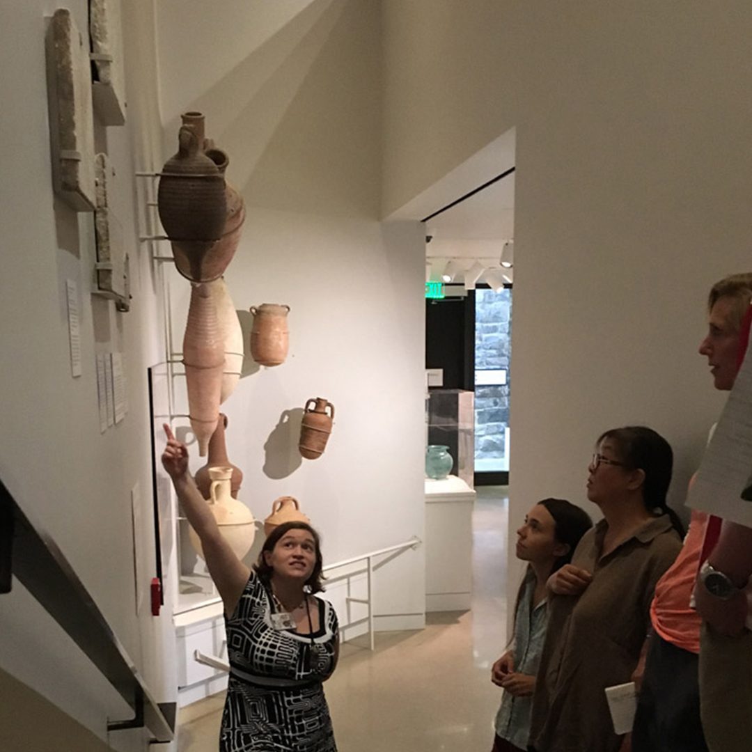 Cathy Person leads a university student tour in the Kelsey Museum’s galleries, pointing to Latin inscriptions mounted on the wall.