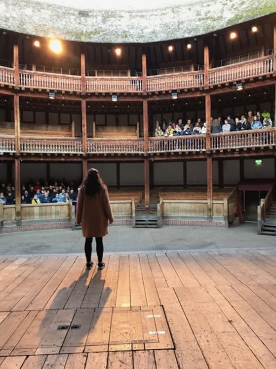 View of Laura's back as she is standing on The Globe stage in London facing the crowd stands