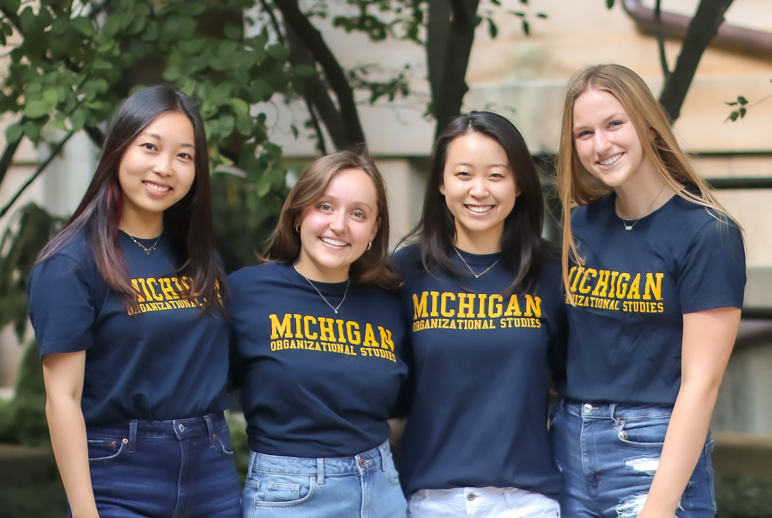4 women smiling at camera in t-shirts that read "Michigan Organizational Studies"