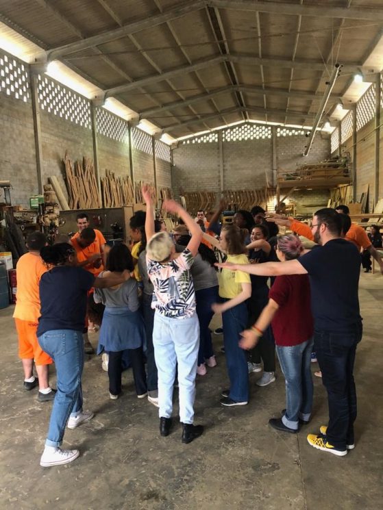 a group of people stand in a circle with their arms raised in a Brazilian prison