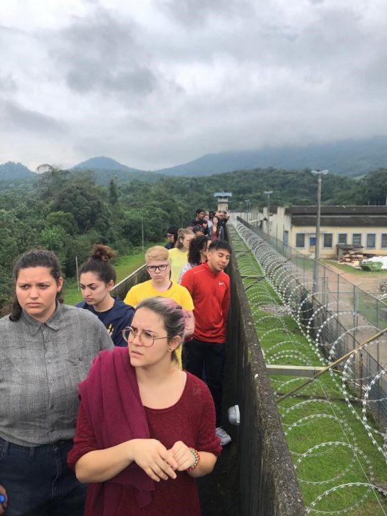 A group of students walks along a perimeter walkway outside a Brazilian prison.