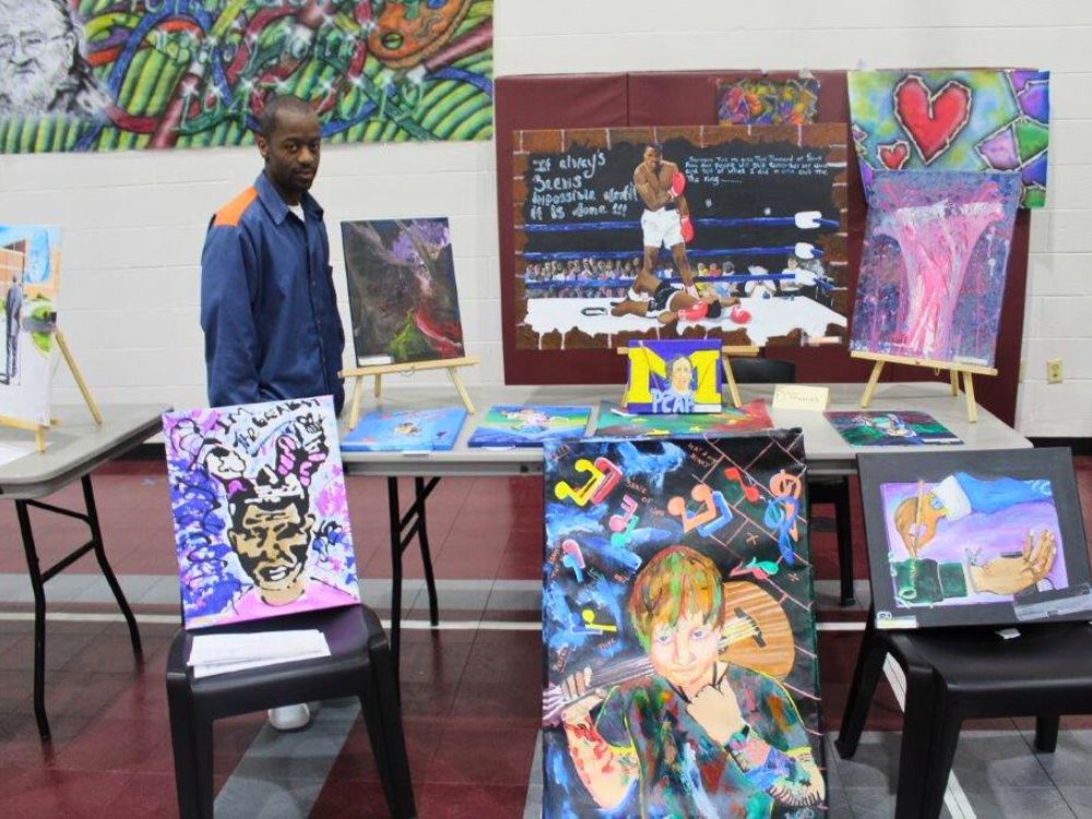Man standing next to a table filled with his colorful painting