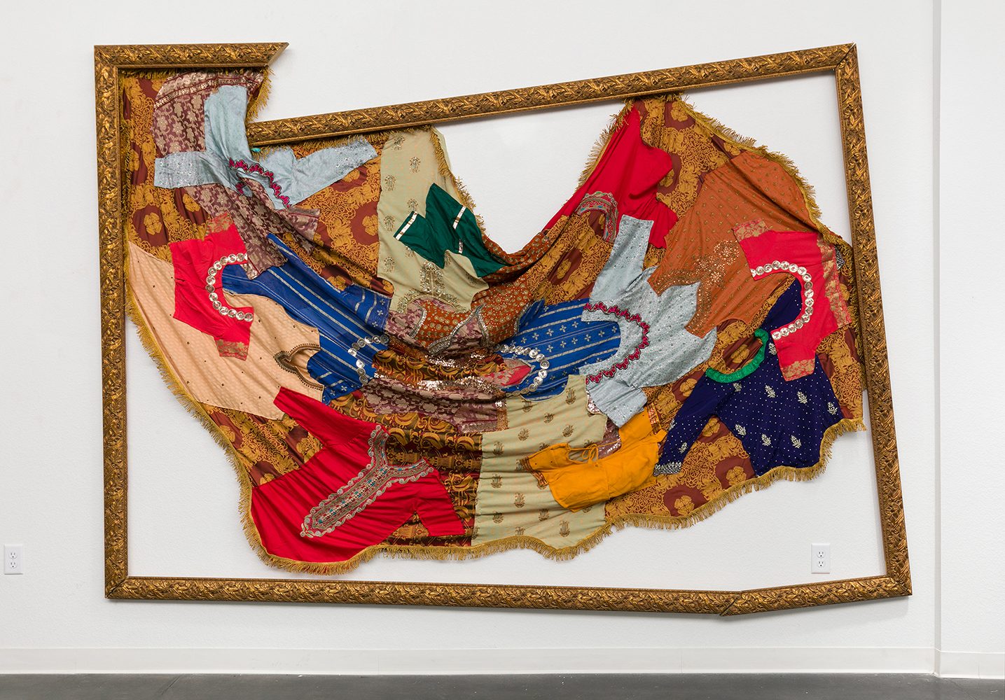 A broken picture frame contains a tattered quilt made of small pieces of clothing