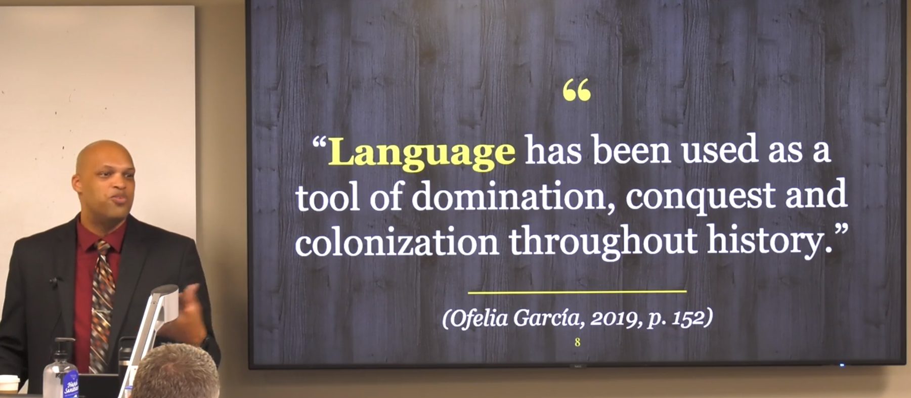 LJ Randolph leads the workshop next to a presentation slide that says, "Language has been used as a tool of domination, conquest and colonization throughout history."