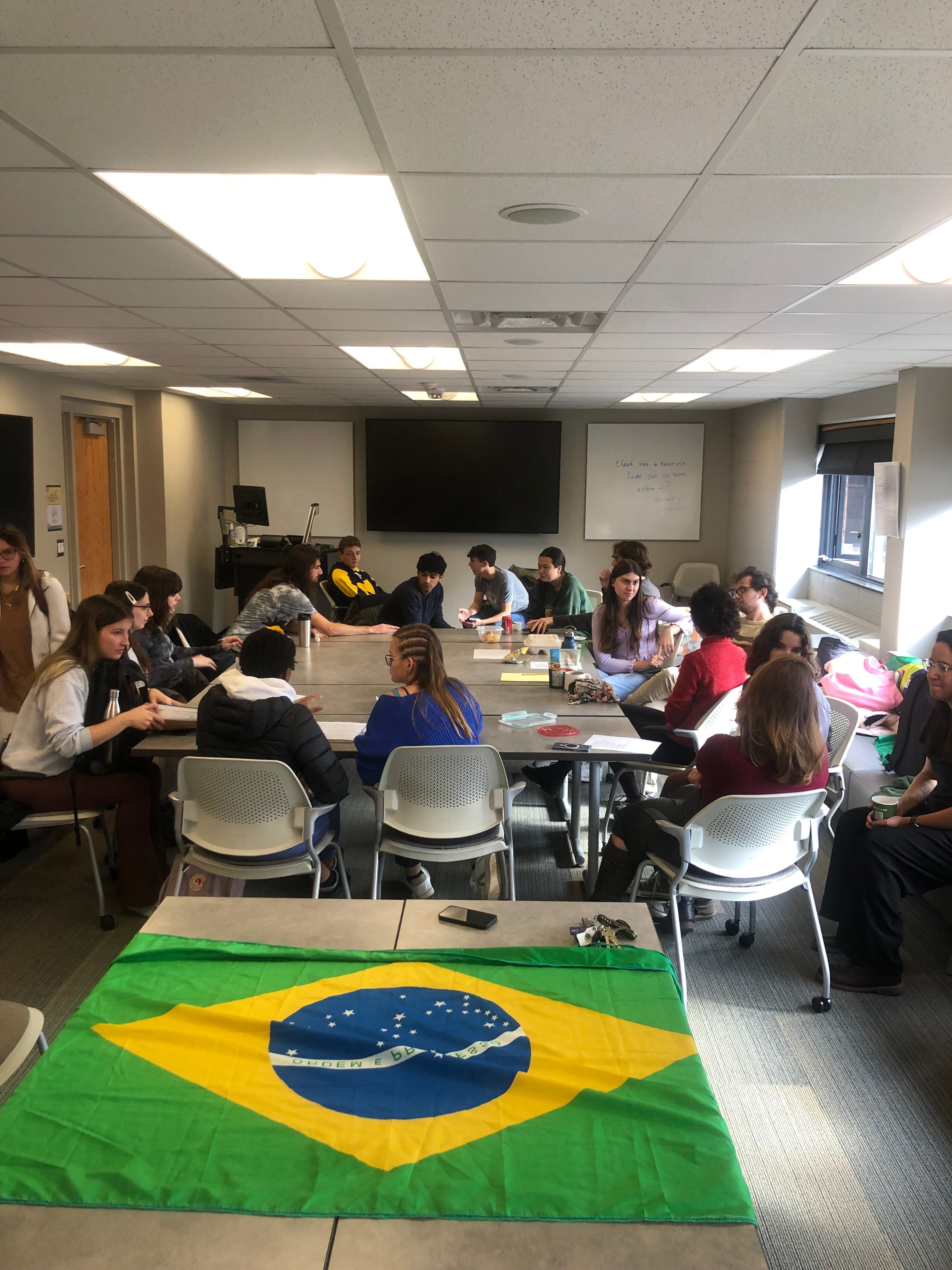 Portuguese Students chat around a table with the flag of Brazil in the forefront