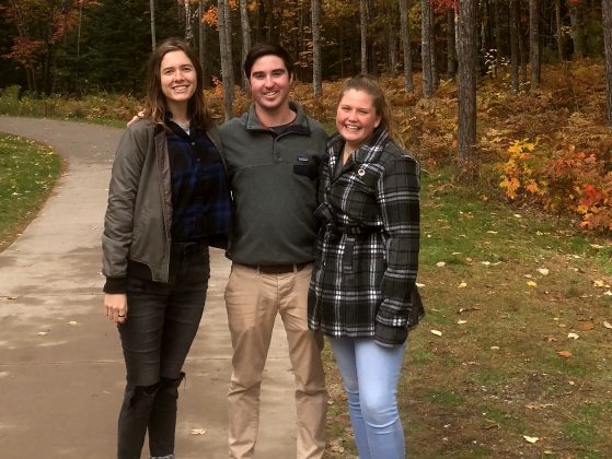 3 students standing together with trees with red and orange leaves behind them