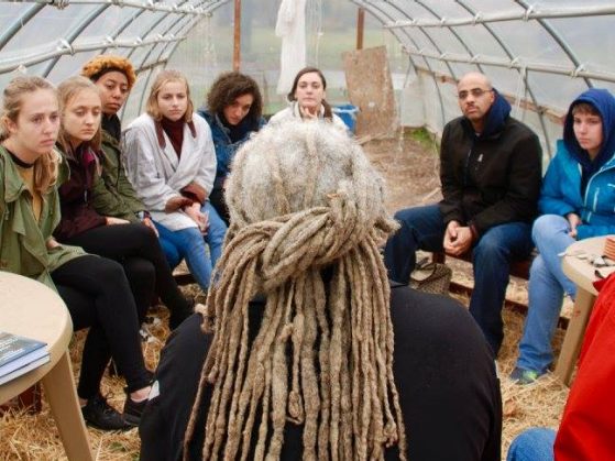 Students sit in hoop house listening intently to man with graying dreadlocks