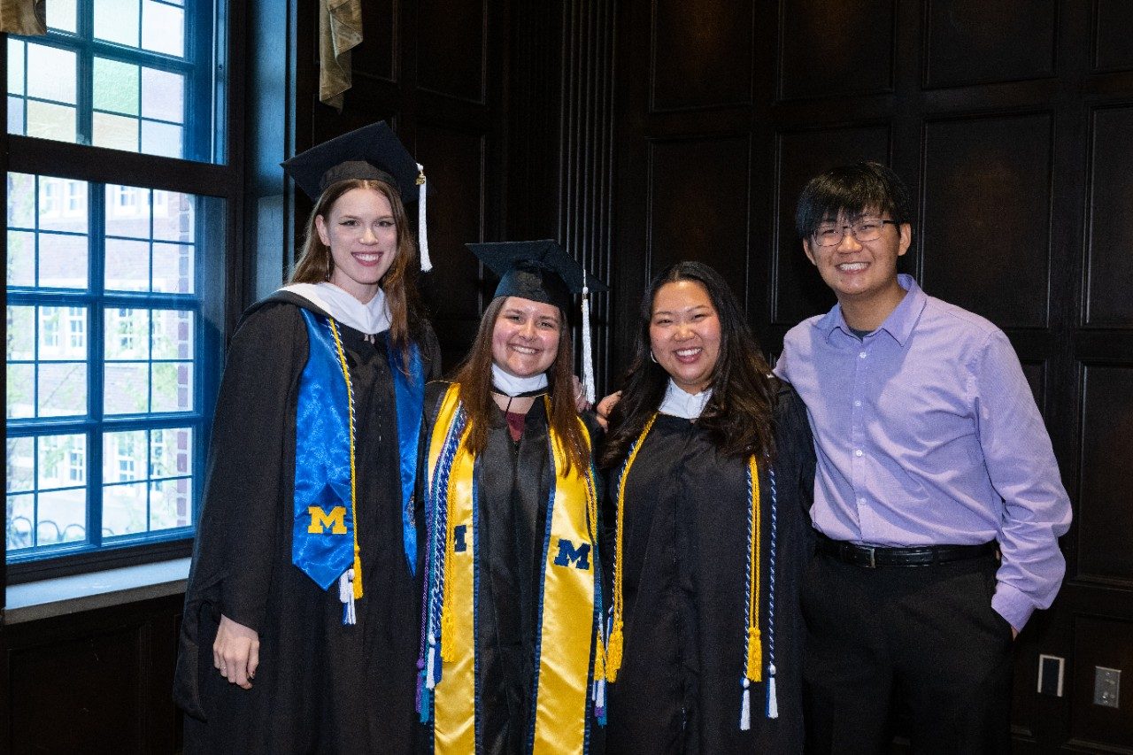 Four students, some wearing caps and gowns, standing next to each other and smiling.
