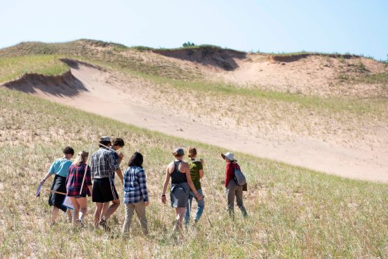 Students trek through the dunes on a sunny day.